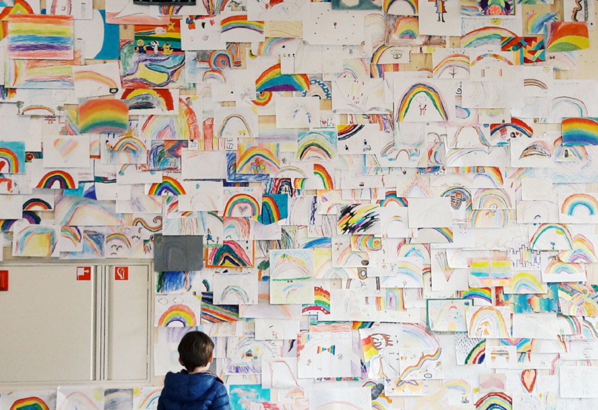 kid-in-colourful-clothes-watching-other-children-drawings-of-a-rainbow