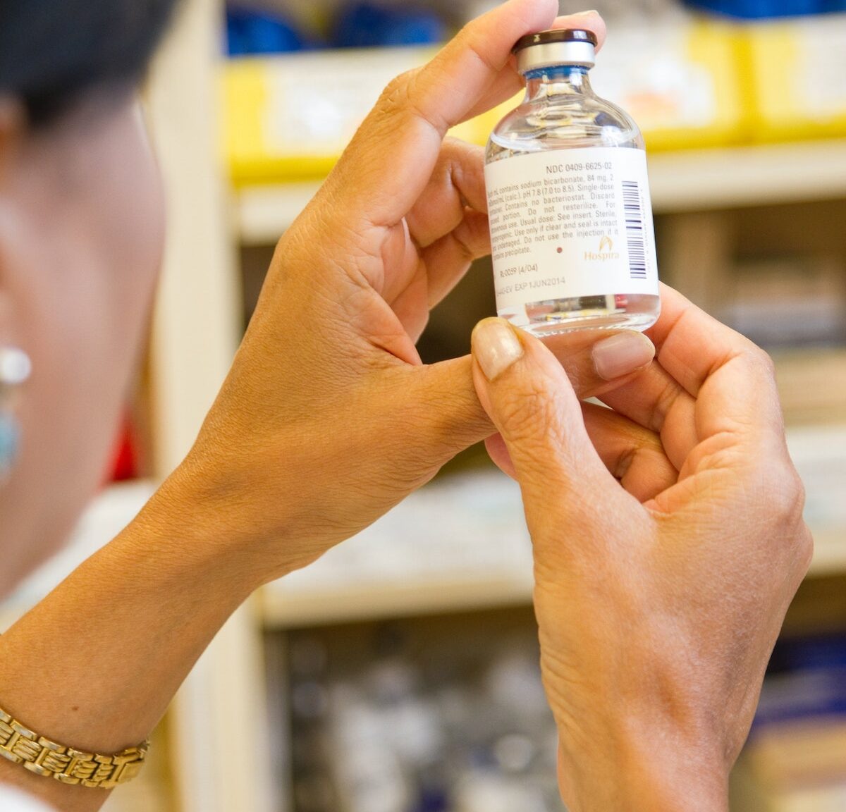 A female pharmacist is examining a vial in a pharmacy.