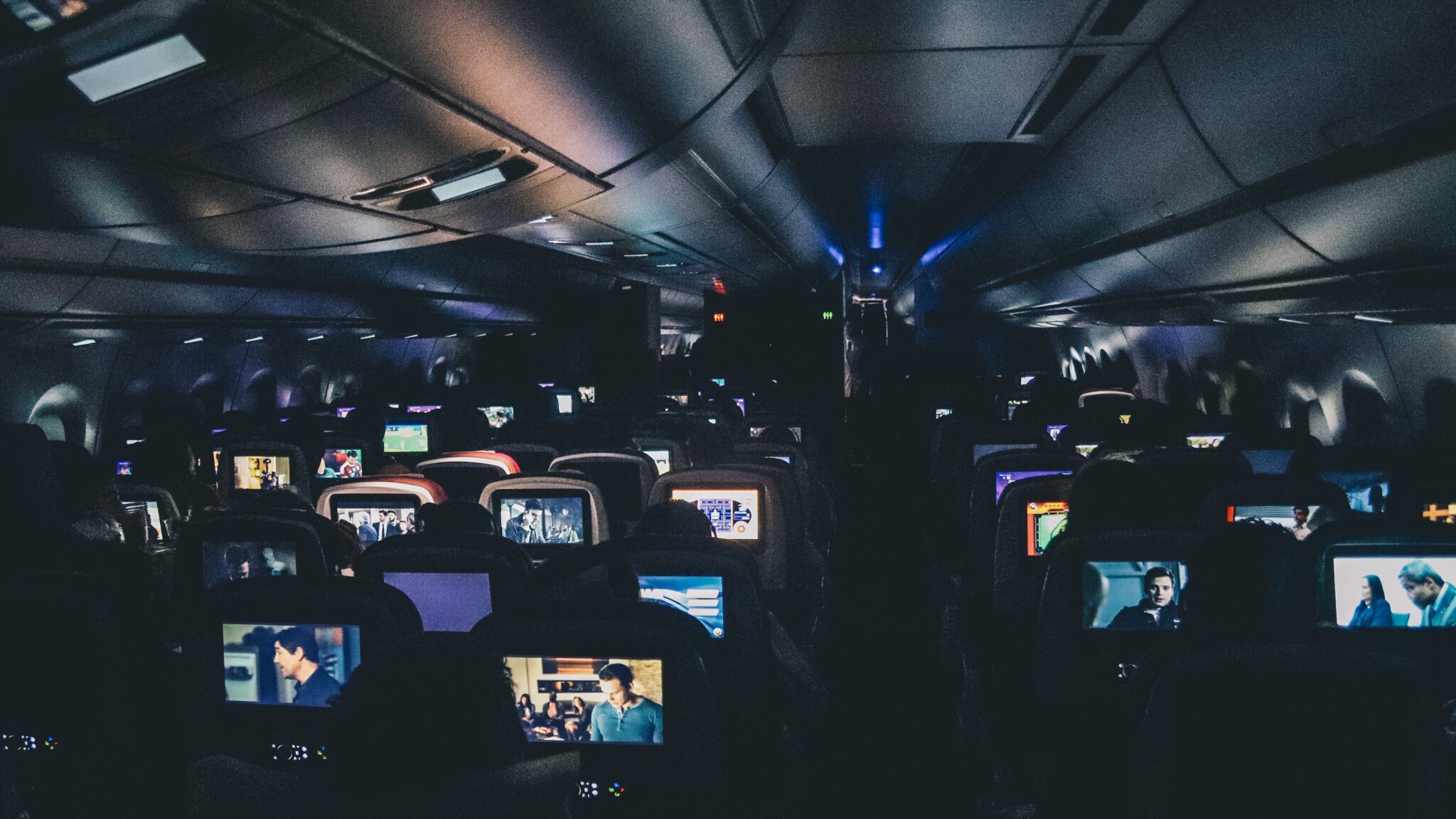 Image from the back of an airplane showcasing all the different forms of entertainment individuals choose on a flight.
