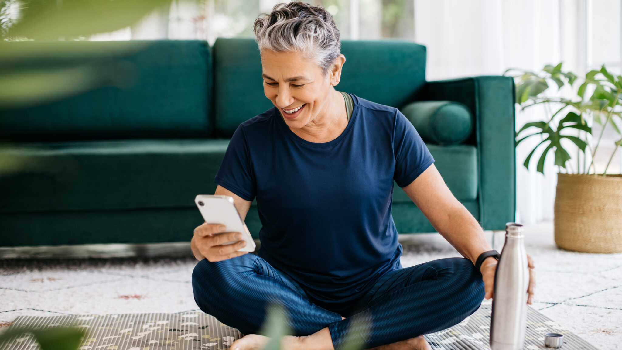 Photograph of a happy senior woman using a smartphone during yoga, tracking her fitness progress on a smart app
